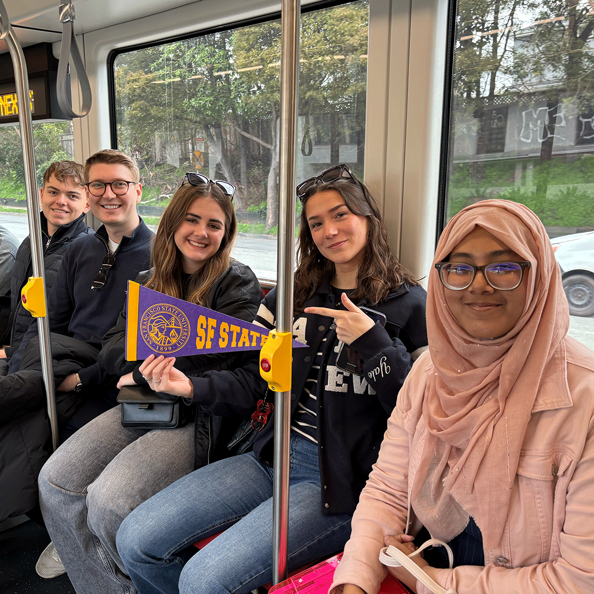 International students riding Muni, holding an SFSU pennant