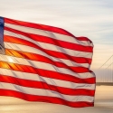 American flag backlit by evening sun and the Golden Gate Bridge in the distance